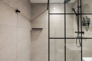 A modern bathroom with a glass shower enclosure, a handheld showerhead, and a wall-mounted faucet.