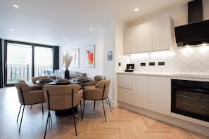 A modern kitchen with white cabinets, a black oven, and a dining area with a round table and chairs. - Urbano | The Heim (Greater Manchester)