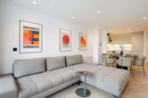 A modern living room with a sectional sofa, a small round table, and a dining area with chairs. - Urbano | The Heim (Greater Manchester)
