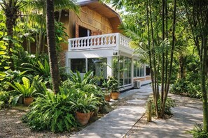 A wooden house with a balcony, surrounded by lush greenery and potted plants.