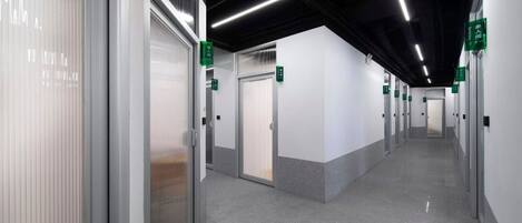 A clean, modern hallway with doors marked by green signs, leading to individual rooms.