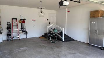 Un garage équipé d’un ventilateur de plafond, d’un projecteur fixé au plafond, d’un vélo avec un panier, d’un coffre pour un déneigeuse et d’une armoire métallique.