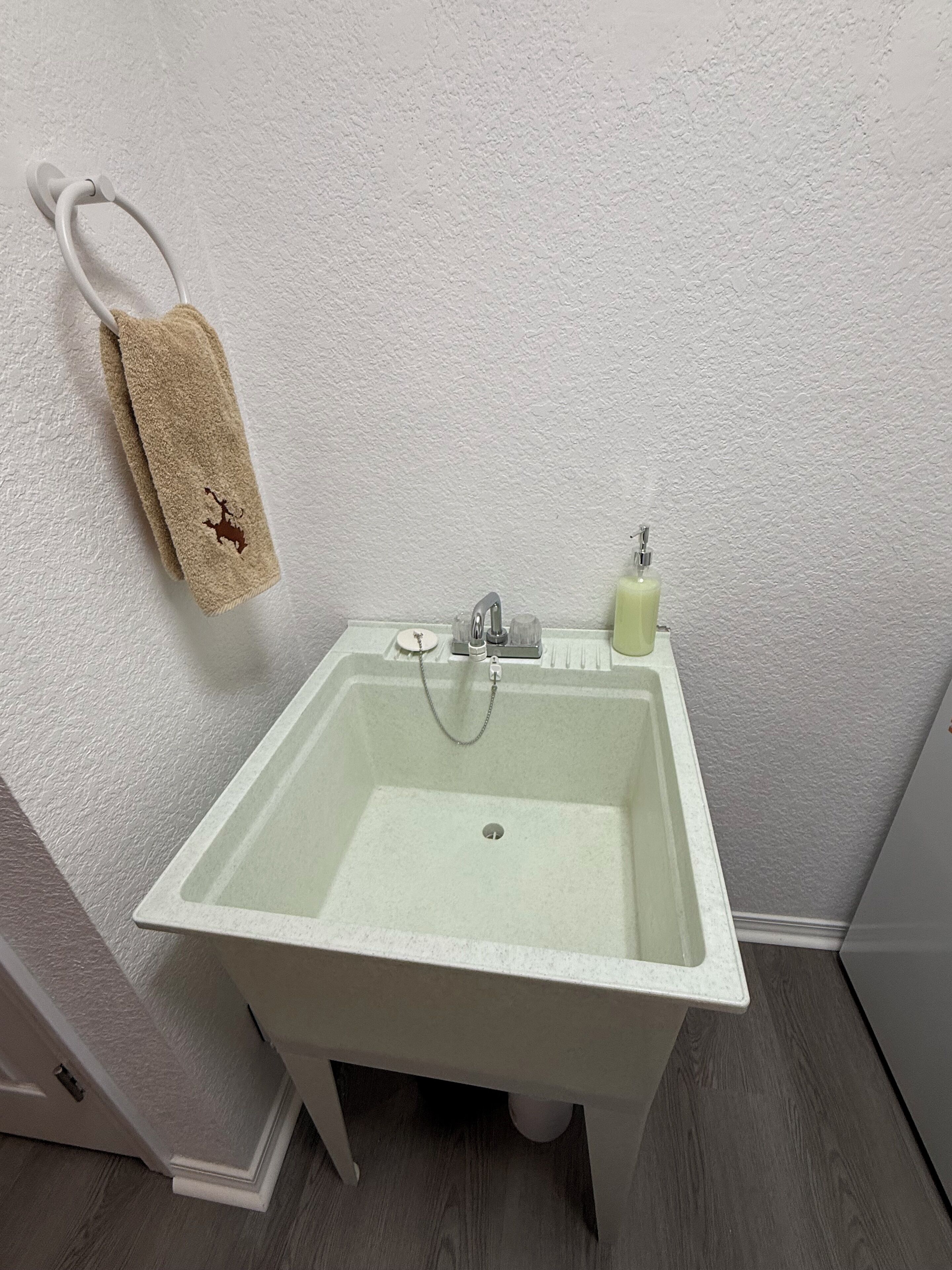 Um banheiro pequeno e branco, com uma pia, um porta-toalhas com uma toalha bege e um dosador de sabonete.