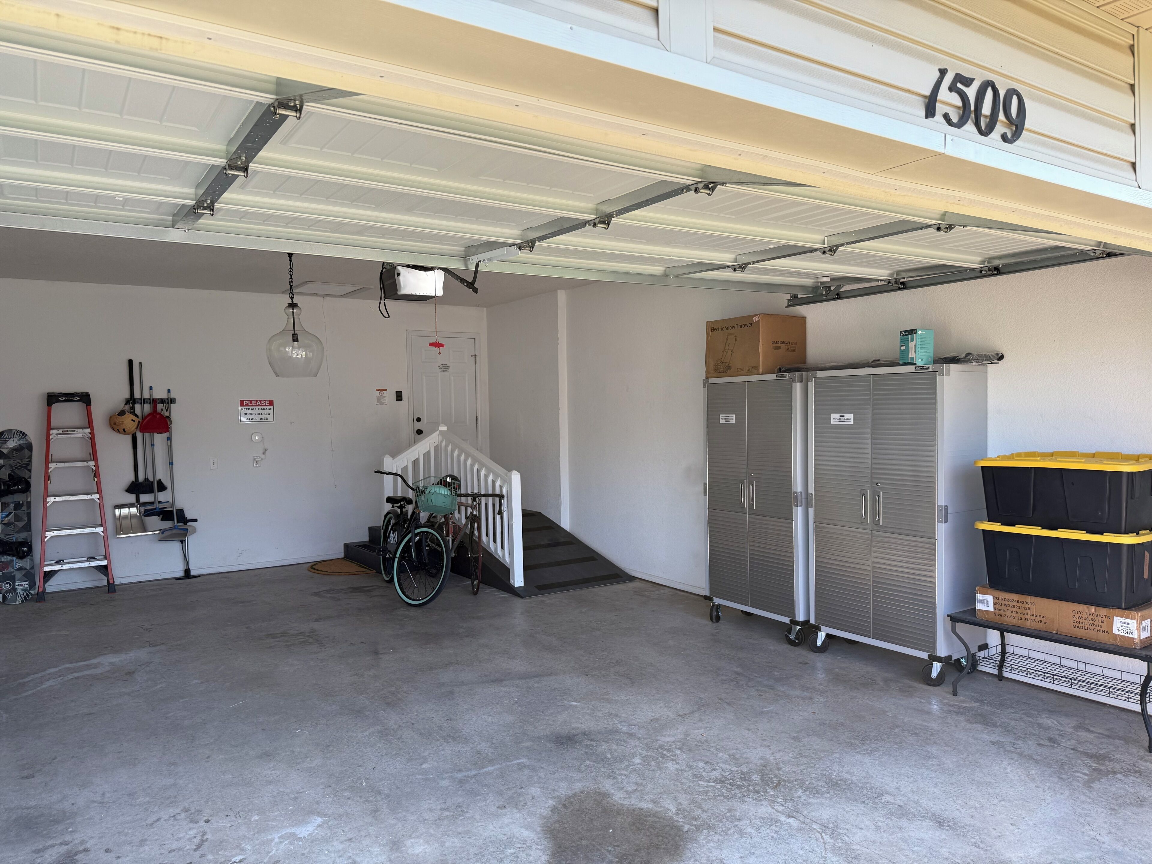 A garage with a concrete floor, a bicycle, a ladder, and a storage cabinet.