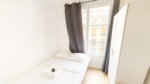 A small, single-bed room with a window, a curtain, and a door.