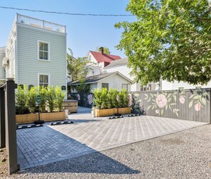 A courtyard with a paved area, a wooden fence with floral designs, and a building with a red roof. - Hot Tub Haven • Parking • Walk to King St! (Charleston)