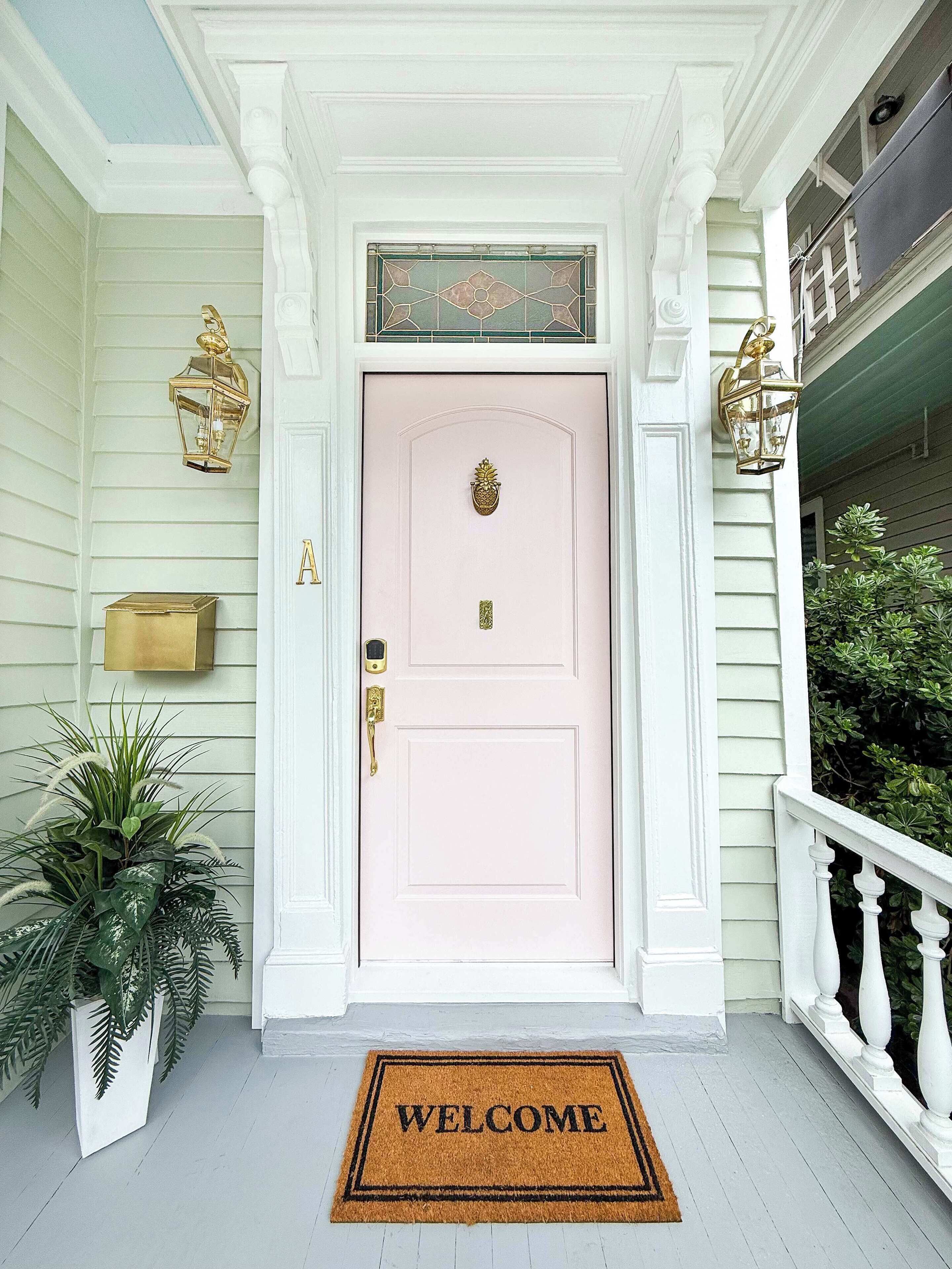 A pink door with a gold knocker, a welcome mat, and a lantern on the porch.