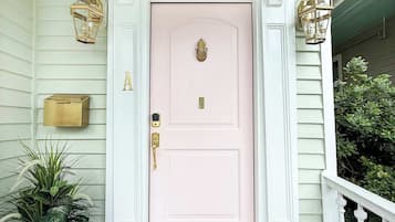 A pink door with a gold knocker, a welcome mat, and a lantern on the porch.