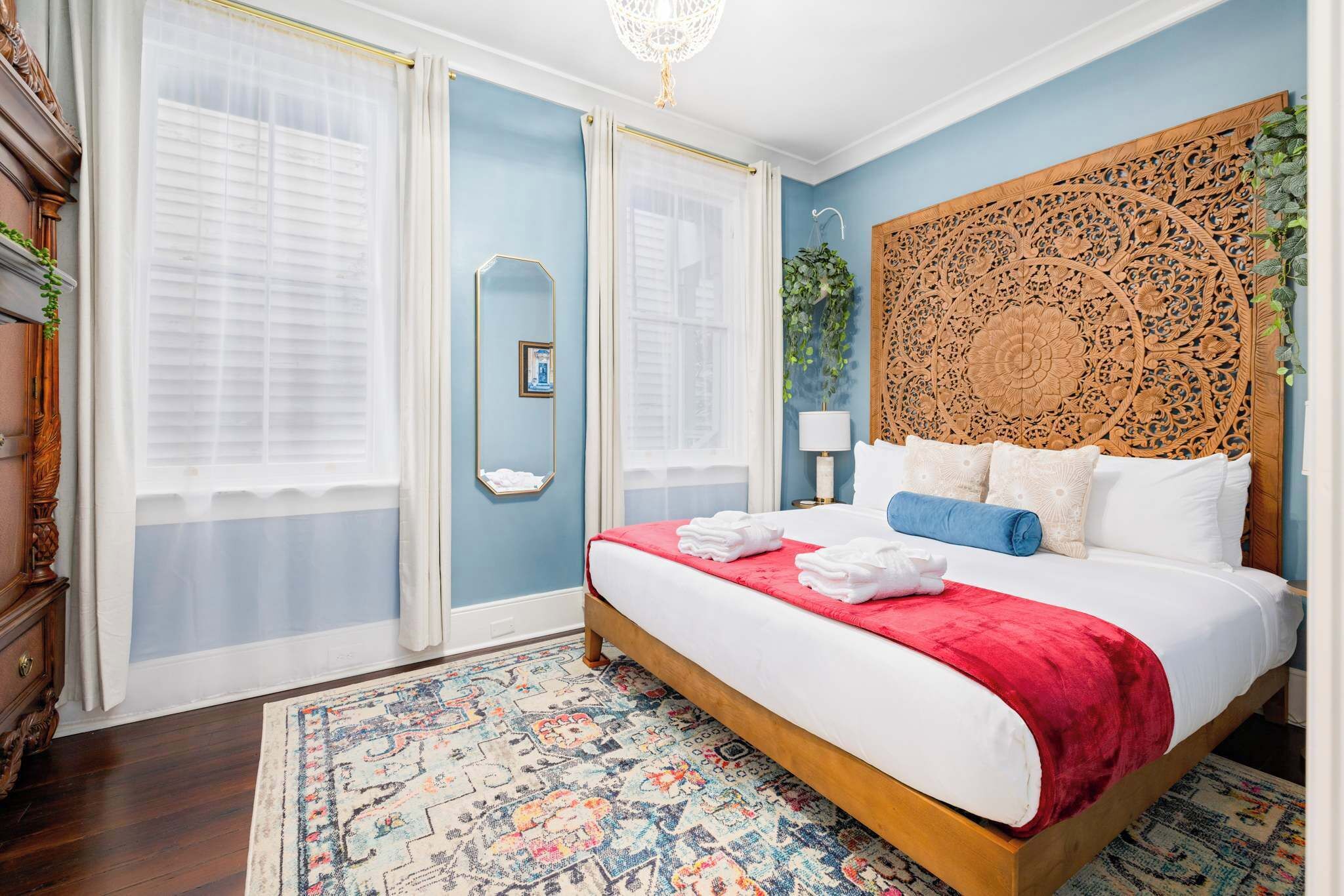 A bedroom with a wooden bed, a red blanket, and a patterned rug.