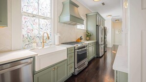 A kitchen with green cabinets, stainless steel appliances, and a window with floral curtains. - Rooftop • Hot Tub • Parking • Walk to King St! (Charleston)