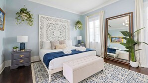 A bedroom with a large bed, a nightstand, a bench, a mirror, and a potted plant. - Rooftop • Hot Tub • Parking • Walk to King St! (Charleston)