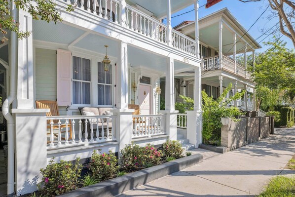 A two-story house with a balcony, a porch with a railing, and a front yard with plants.