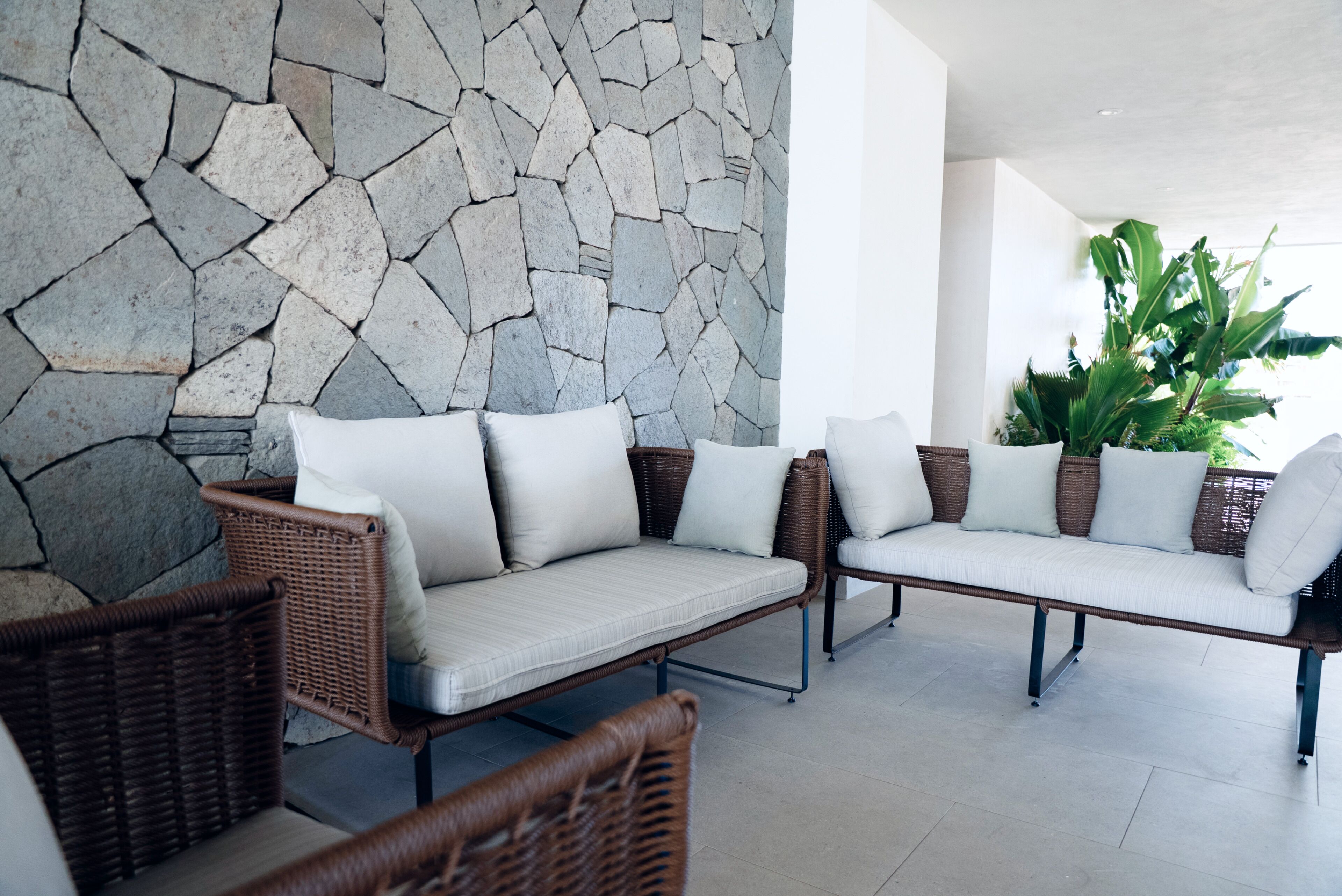 Un muro de piedra, muebles de mimbre y una planta en maceta.