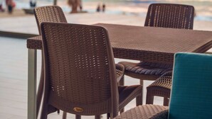 A wicker table and chairs on an outdoor patio with a view of the ocean and beach in the background. - Avenir Armonia Suites (Rincón de Guayabitos)