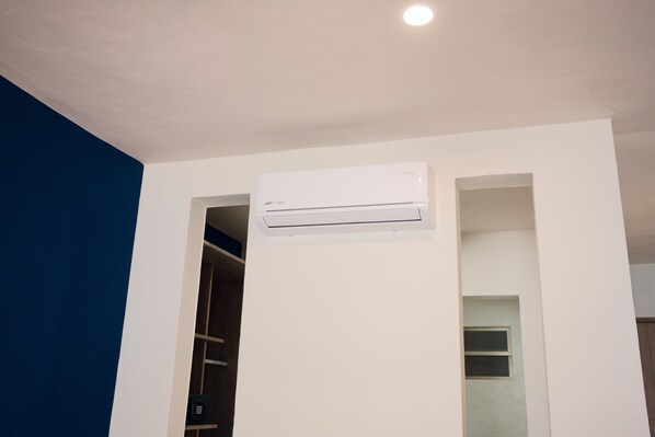 Una habitación con un equipo de aire acondicionado blanco instalado en la pared, una puerta de madera y un techo blanco.