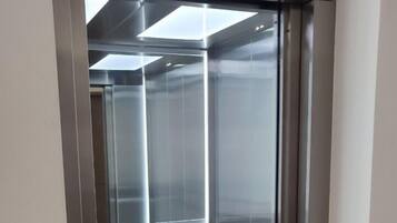 A modern elevator with metallic walls and a glass door, part of a building with a minimalist design.