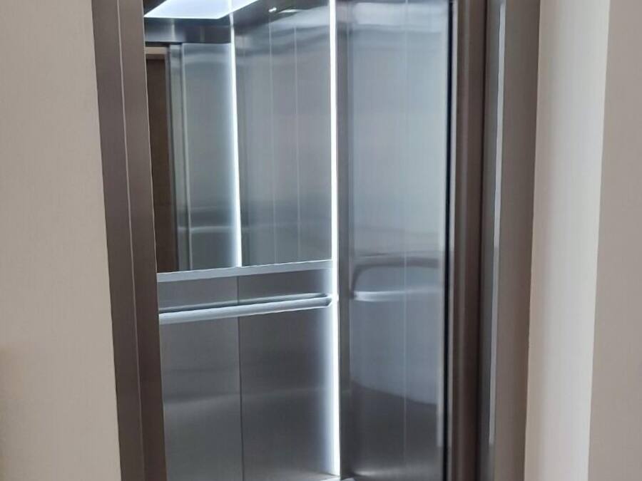 A modern elevator with metallic walls and a glass door, part of a building with a minimalist design.