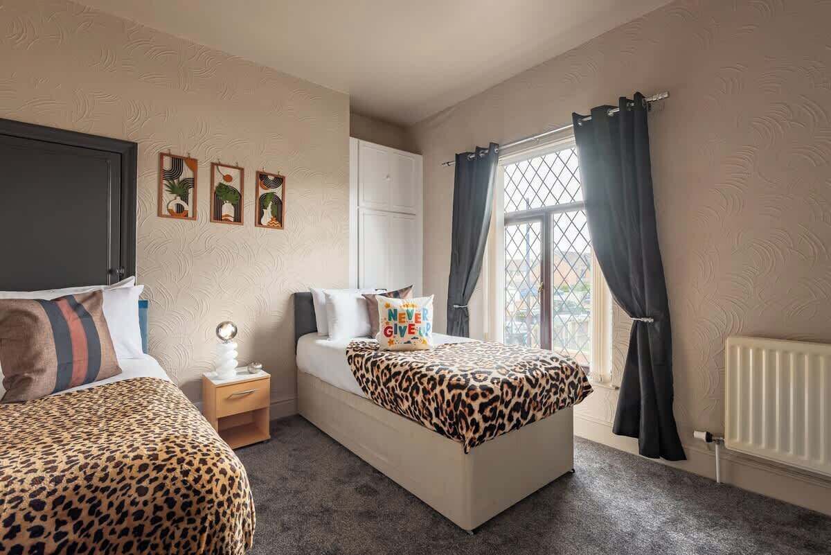 Une chambre à coucher avec un lit, une table de chevet, une commode et une fenêtre avec des rideaux.