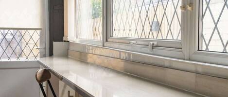 A kitchen with a white countertop, two bar stools, and a window with a diamond-patterned screen.