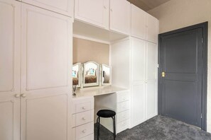 A room with a white vanity, a mirror, and a black stool. There is a dark door to the right. - Quiet Garden Home w/ Free Street Parking & Fast WiFi (Kingston upon Hull)
