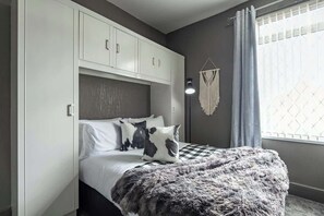 Ein Schlafzimmer mit einem Bett, weißen Schränken, einem Wandbehang aus Makramee und einem Fenster mit Vorhängen.