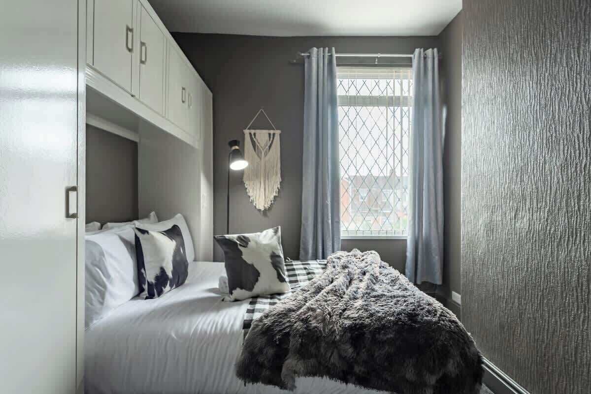 Un dormitorio con cama, decoración de macramé en la pared y una ventana con cortinas.
