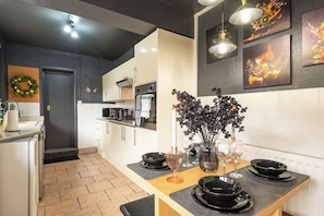A modern kitchen with a dining area, featuring a central island with black plates and a vase of flowers. - Quiet Garden Home w/ Free Street Parking & Fast WiFi (Kingston upon Hull)