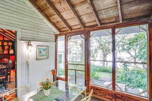 Un plafond en bois, une table en verre avec des chaises, et une vue sur la verdure à l’extérieur.