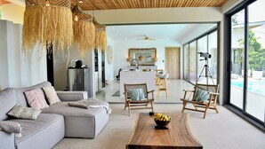 A modern living room with a sofa, wooden coffee table, wicker chairs, and a kitchen in the background.