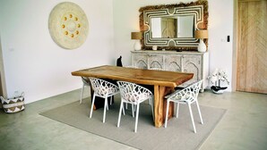 A dining area with a wooden table and white chairs, a decorative mirror, and a patterned wall hanging.