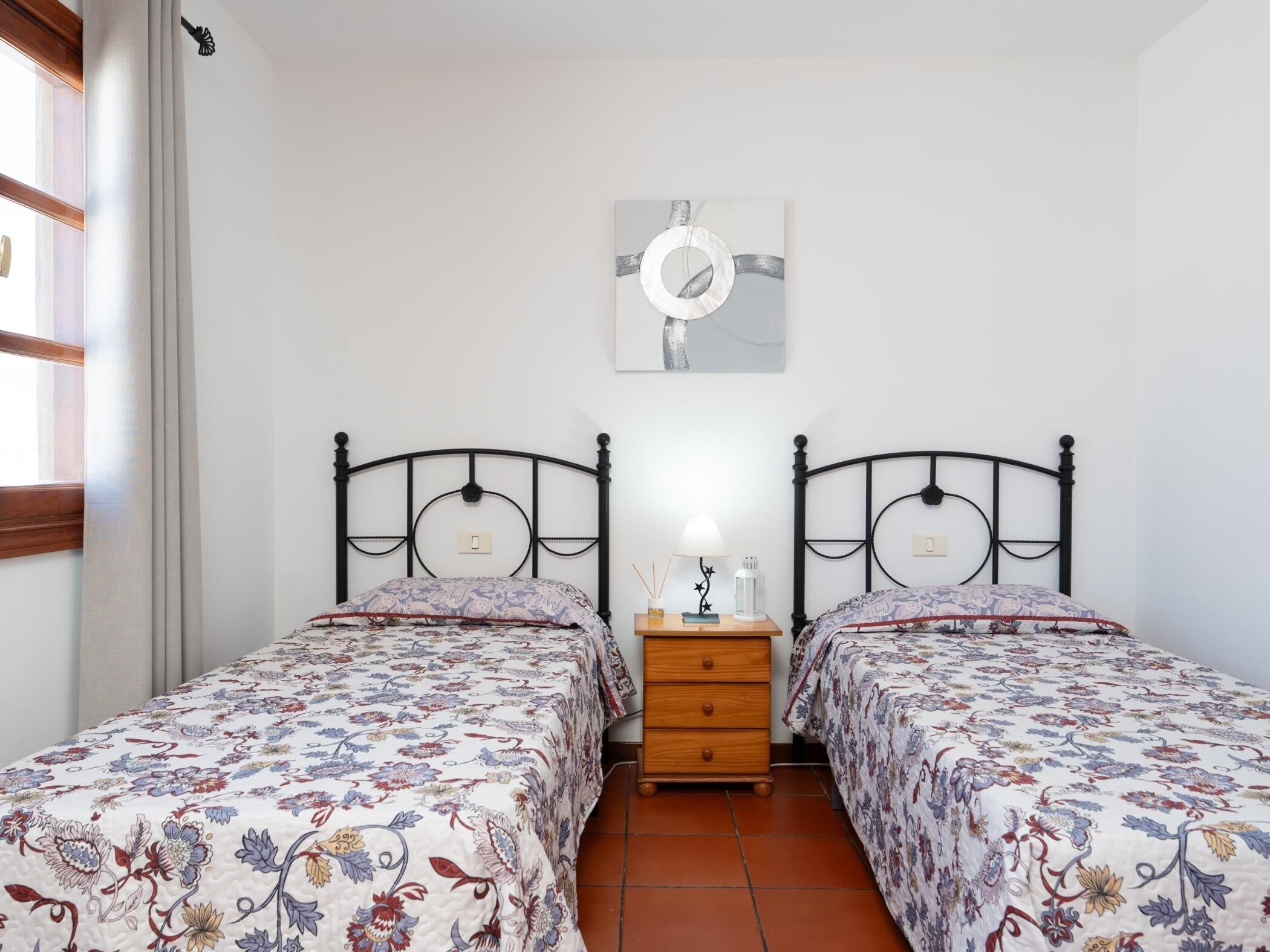 Een slaapkamer met twee bedden, een nachtkastje, een lamp en een kunstwerk aan de muur.