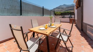 Une terrasse avec une table dressée pour deux personnes, des chaises et une vue sur les montagnes.