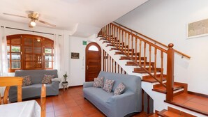 Un hall d’hôtel avec un escalier en bois, un canapé gris, une table en bois et un ventilateur de plafond.