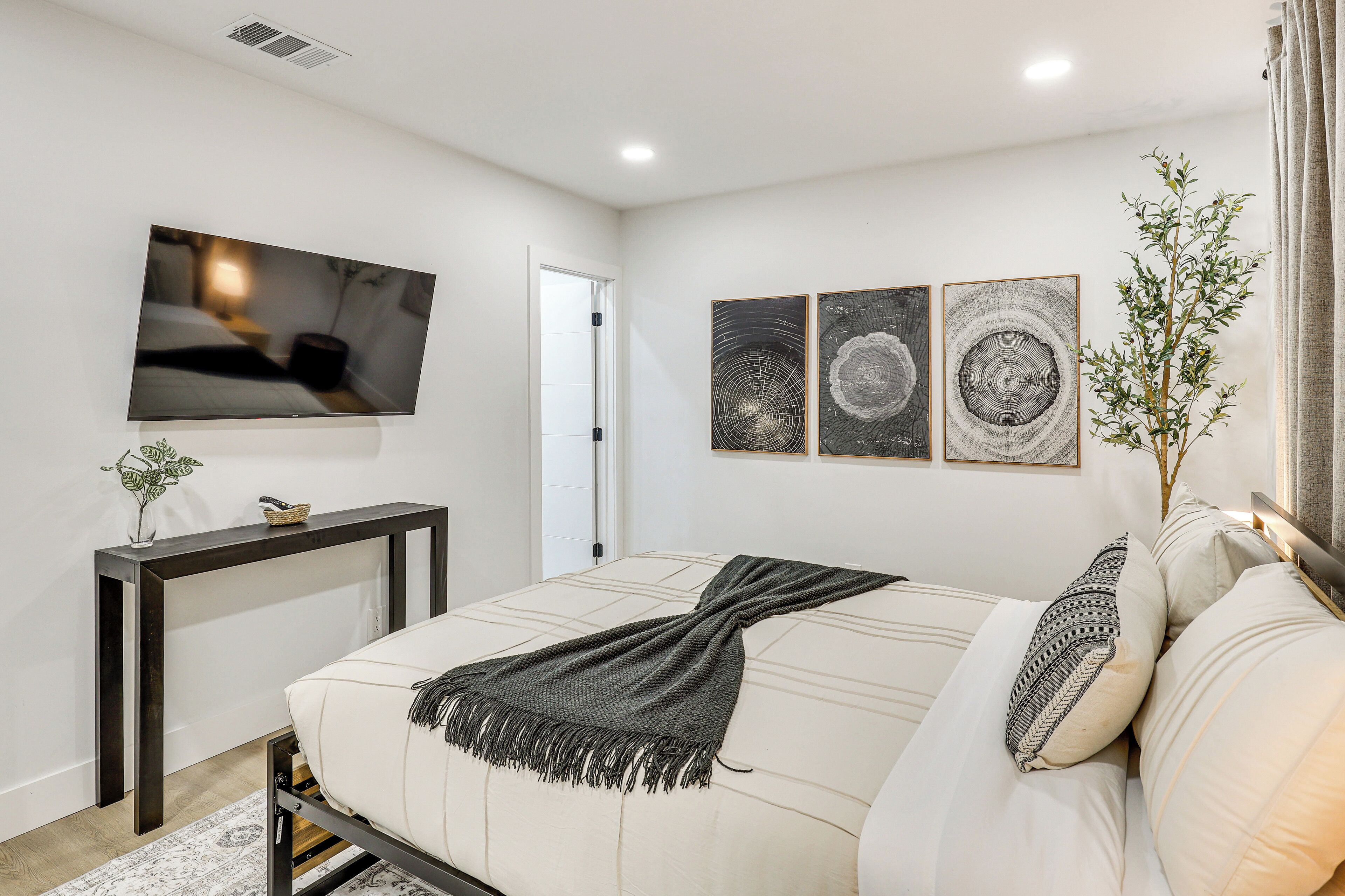 A modern bedroom with a bed, a TV mounted on the wall, and three framed artworks.