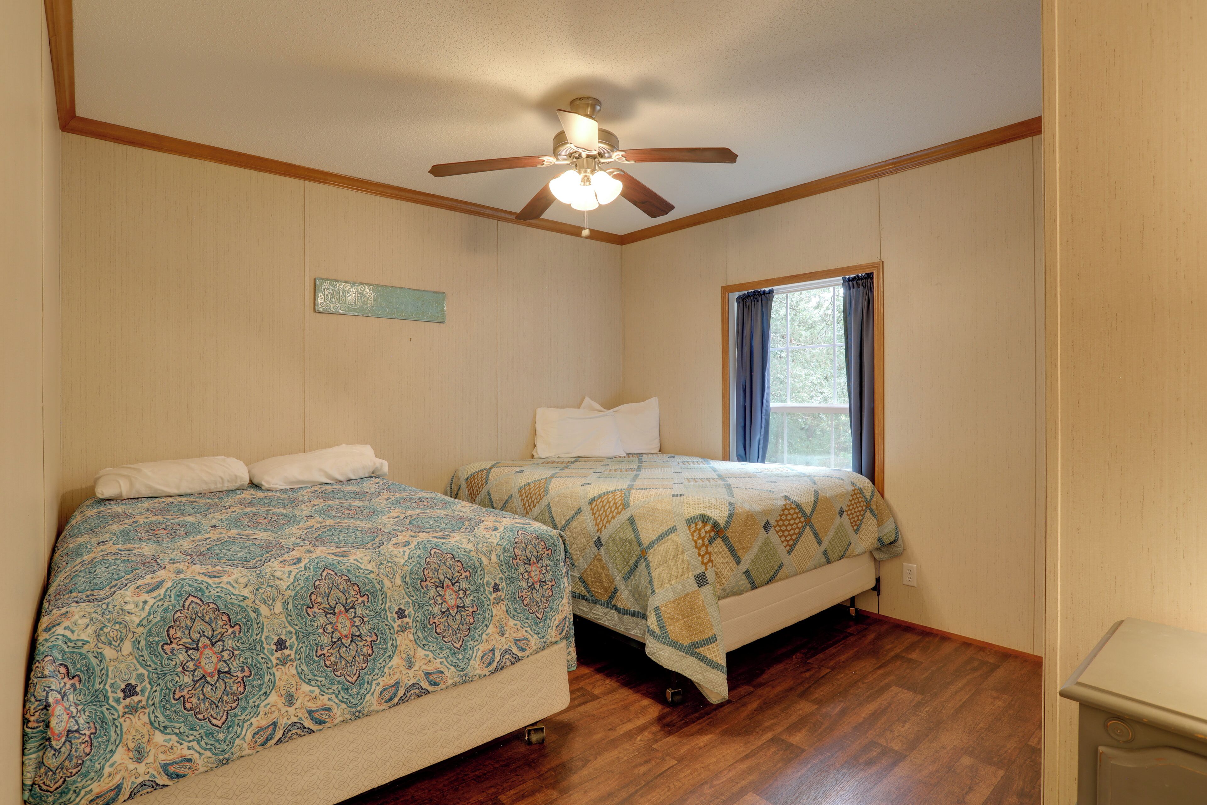 Une chambre avec deux lits, un plancher en bois, un ventilateur de plafond et une fenêtre avec des rideaux.