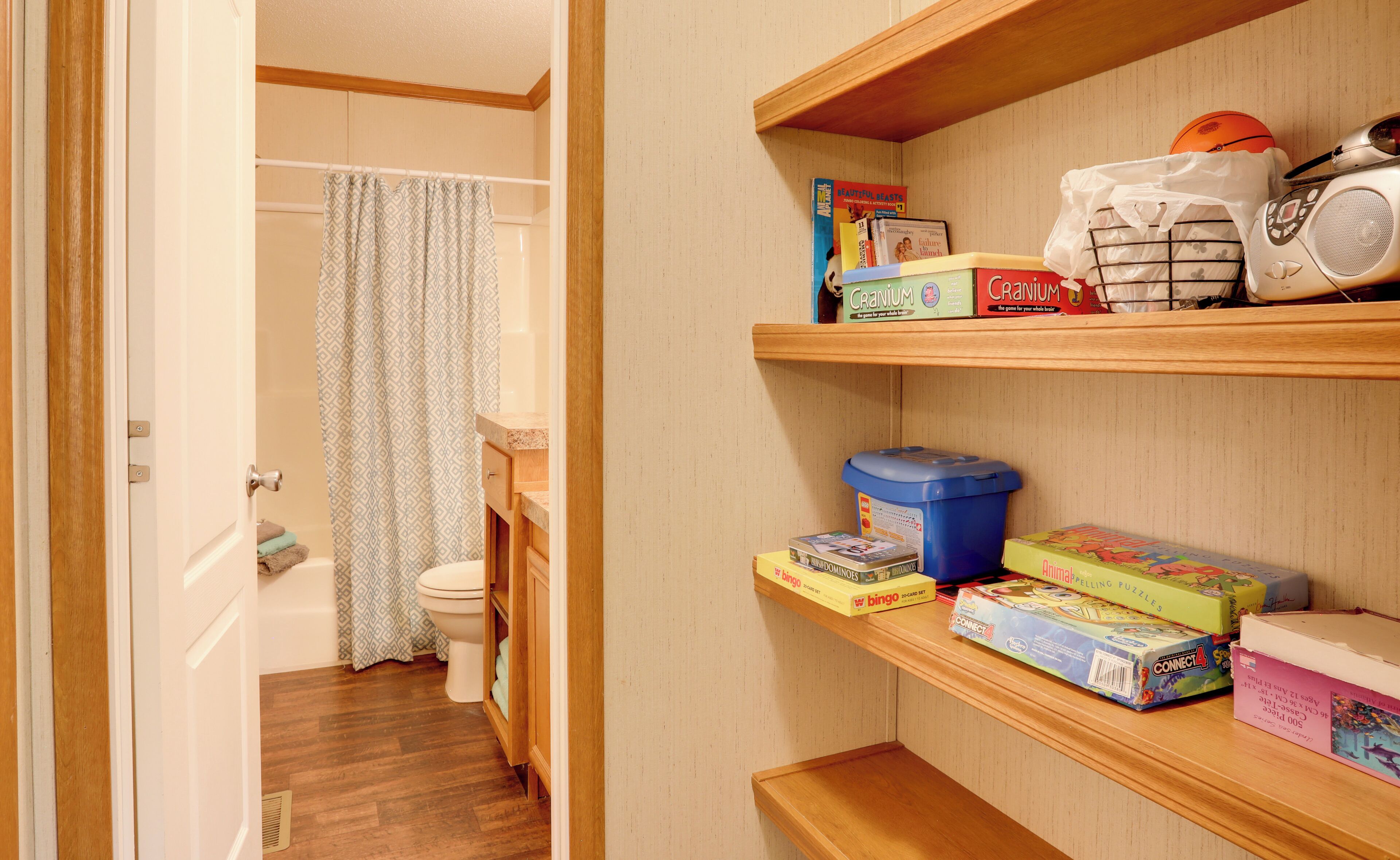 A bathroom with a shower curtain, toilet, and wooden shelves with various items.