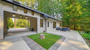 A modern house with a patio area, a stone feature, and a view of the surrounding forest.