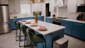 Una cocina moderna con una isla central, armarios azules, electrodomésticos de acero inoxidable y taburetes de bar verdes.