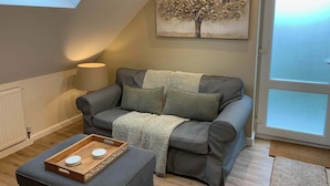 A cozy living room with a grey sofa, a wooden tray with a white object, a lamp, and a painting of a tree. - The Frog, Langport Luxury (Huish Episcopi)