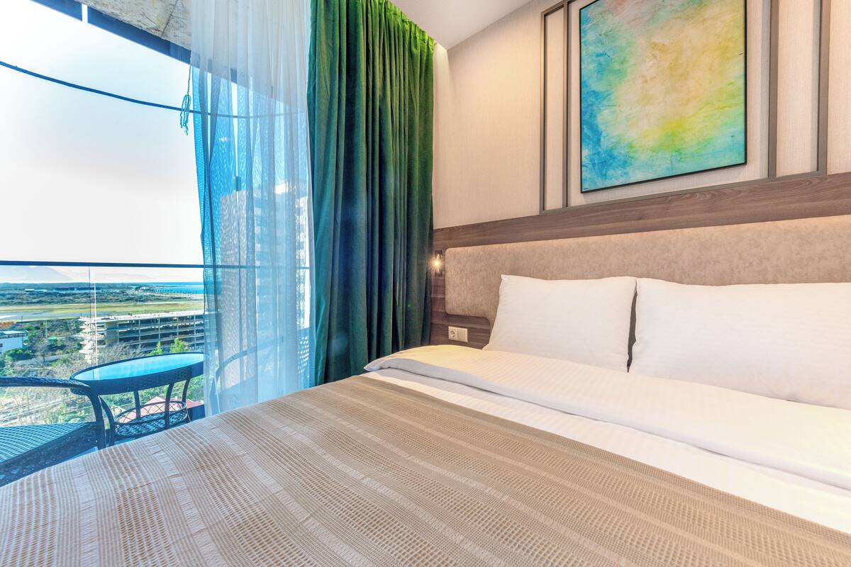 A hotel room with a large bed, a view of the landscape, and a balcony with a table.
