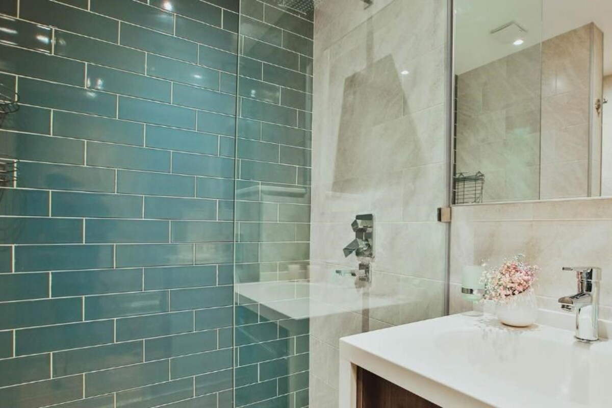 A modern bathroom with a glass shower enclosure, a white sink, and a large mirror.
