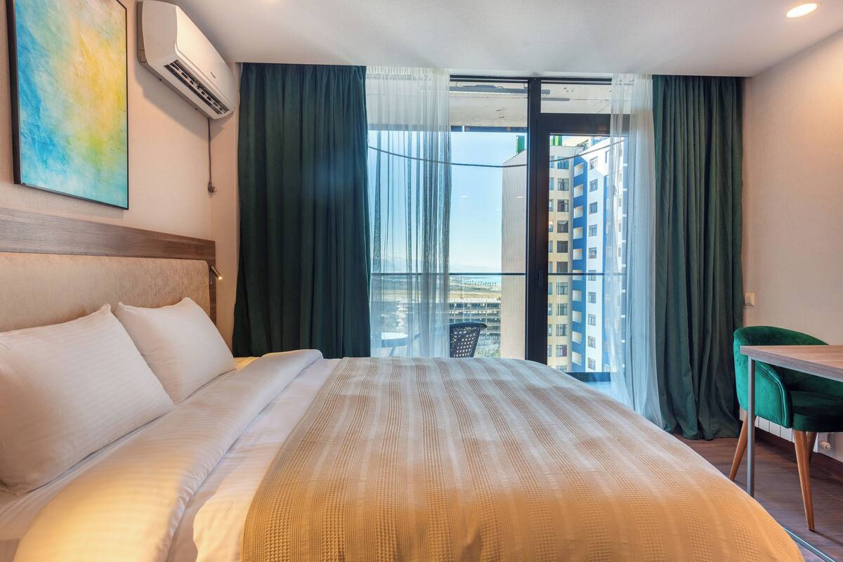 A hotel room with a large bed, a view of a balcony, and an air conditioning unit mounted on the wall.