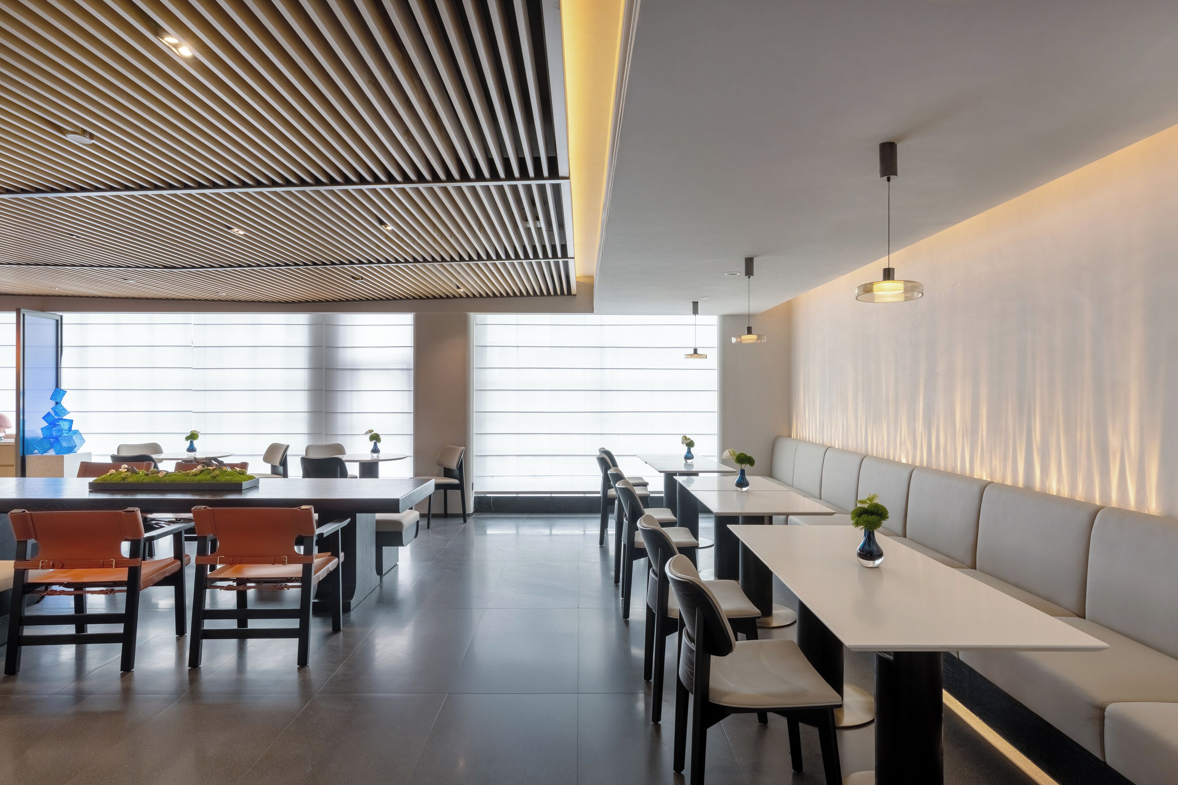 Un comedor moderno con mesas altas y bancos, ventanas amplias y un diseño de techo con listones.