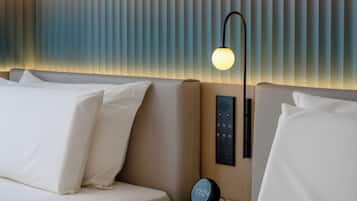 A modern hotel room with a bed, a bedside table with a clock, a wall-mounted control panel, and a wall-mounted lamp.