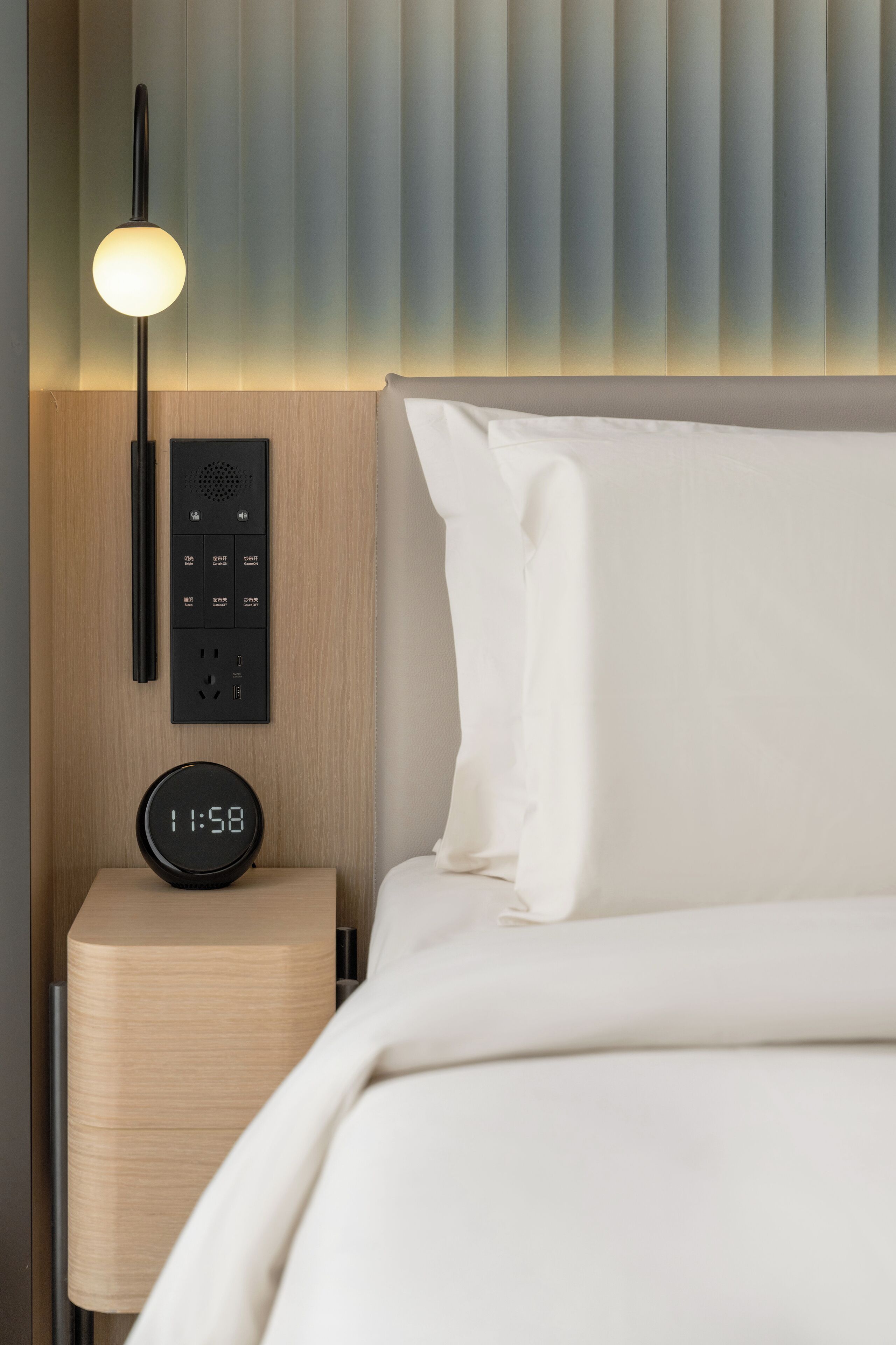 Una habitación de hotel moderna con una cama, una mesita de noche con un reloj digital, una lámpara y un panel de control.