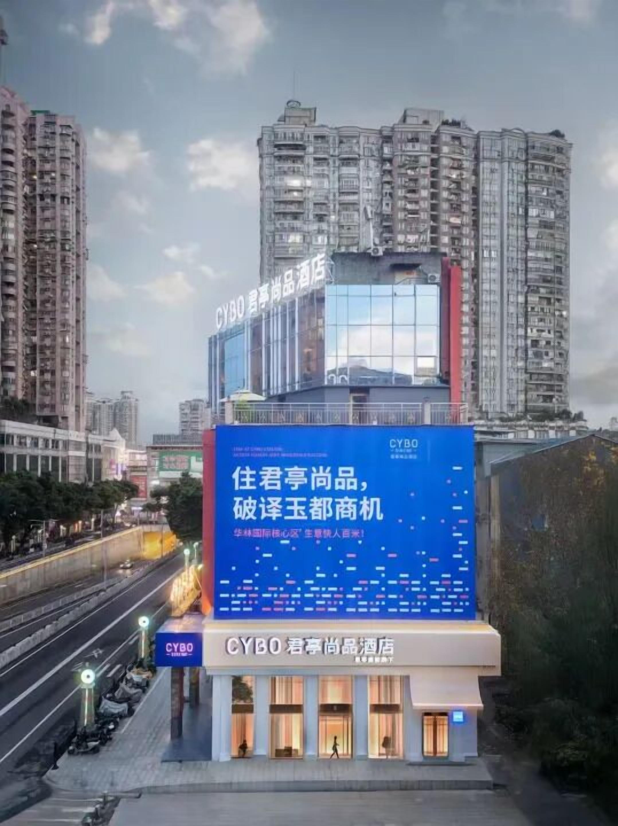 Ein Hotel mit einer großen digitalen Werbetafel, moderner Architektur und Blick auf eine belebte Straße.