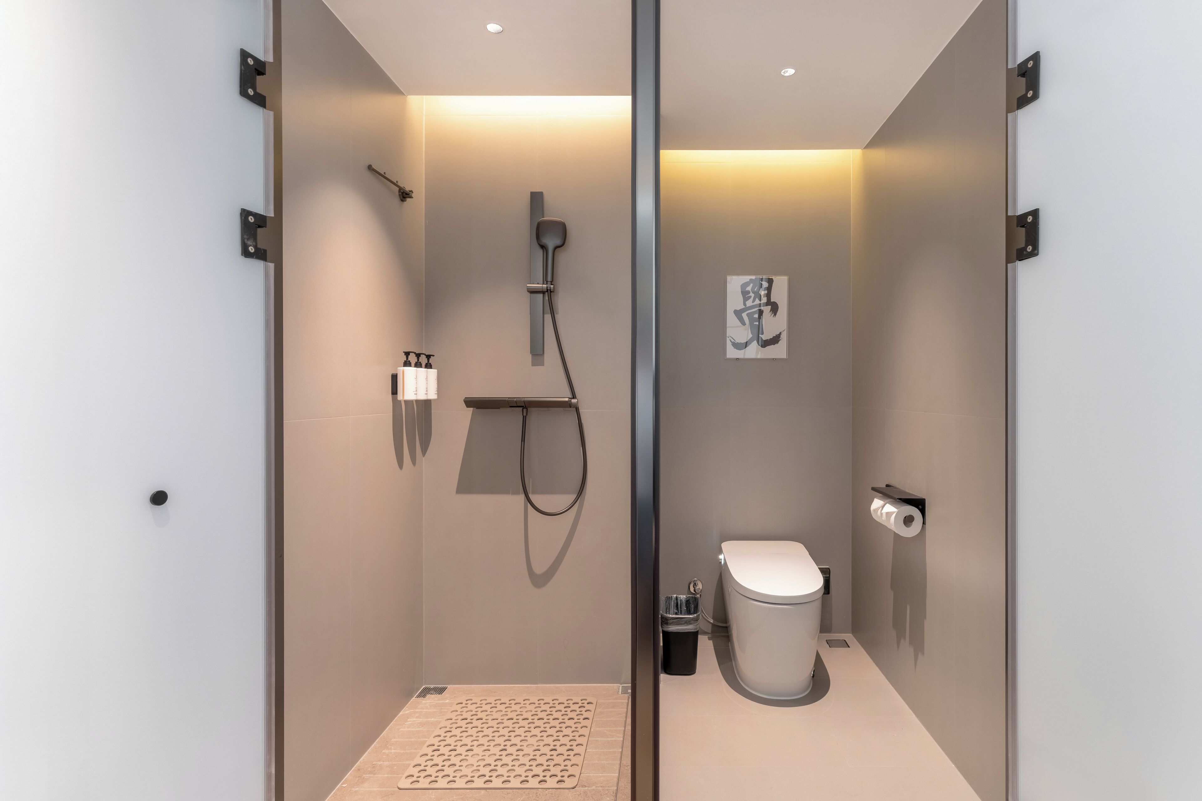 Un baño moderno y funcional con mampara de vidrio, ducha con cabezal de mano, inodoro y un cubo de basura pequeño.