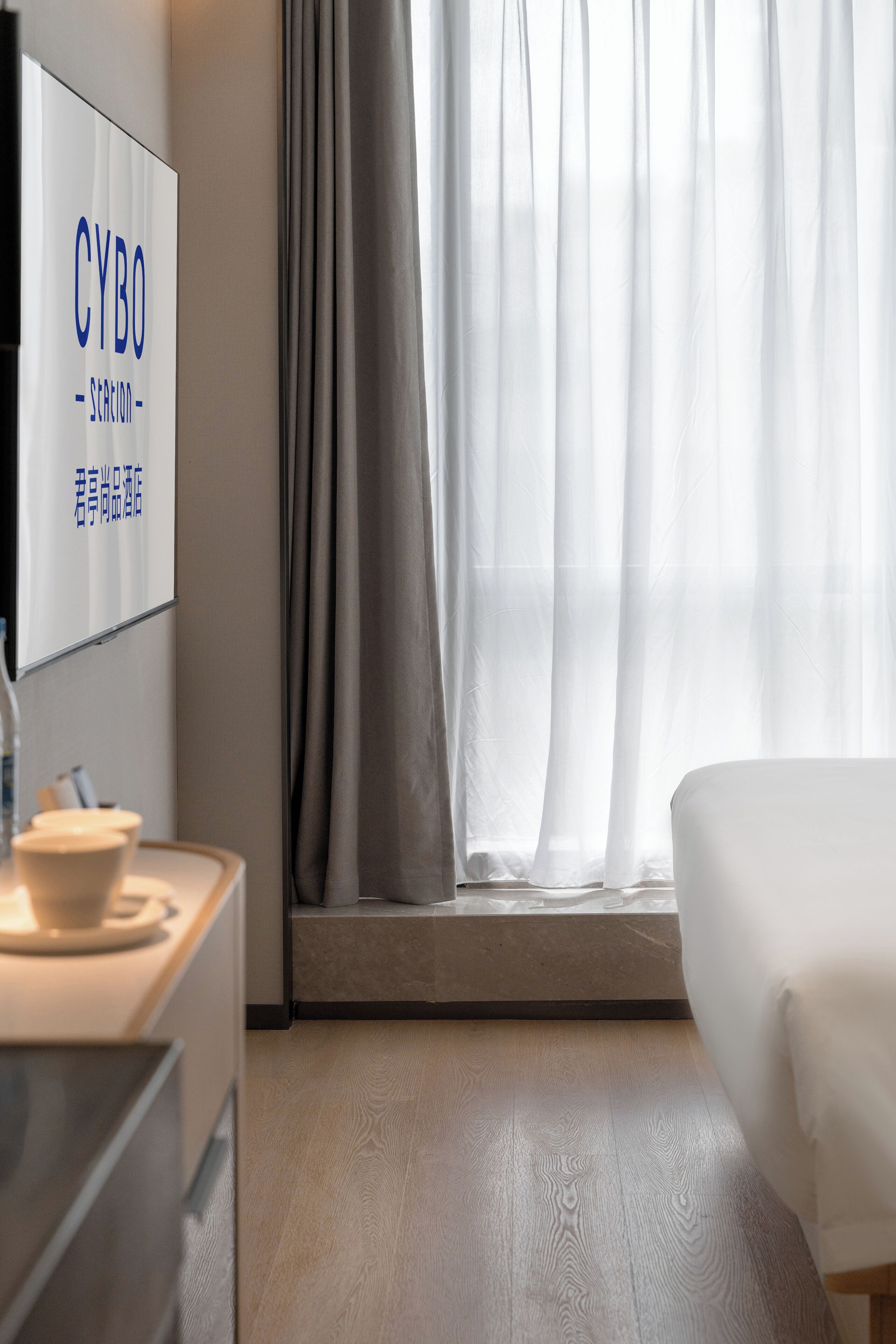 A hotel room with a bed, a desk with a cup, and a window with curtains.
