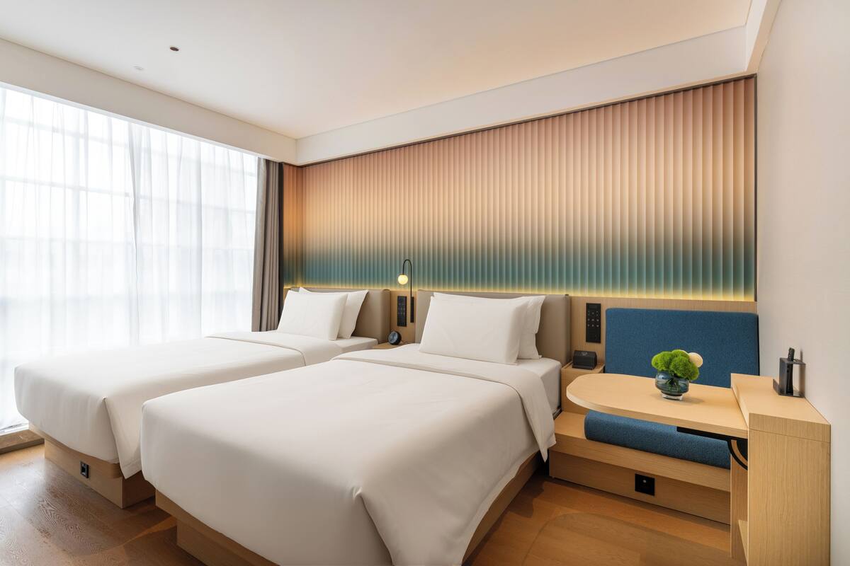 Ein modernes Hotelzimmer mit zwei Betten, einem Schreibtisch und einem großen Fenster.