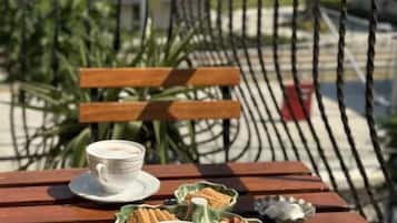 Ein Holztisch mit zwei Kaffeetassen und einer Schüssel mit Snacks auf einem Balkon mit Blick auf ein Gewässer und Gebäude.
